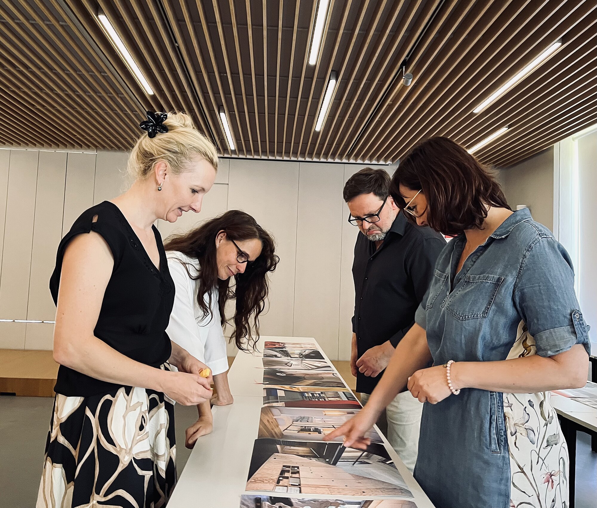 Die Jury v.l.n.r. Henriette Weber, Nadine Merkla, David Nuglisch und Manja Richter (Architektenkammer Sachsen) Vier Personen stehen an einem Tisch und betrachten gemeinsam mehrere ausgebreitete Fotos oder Drucke